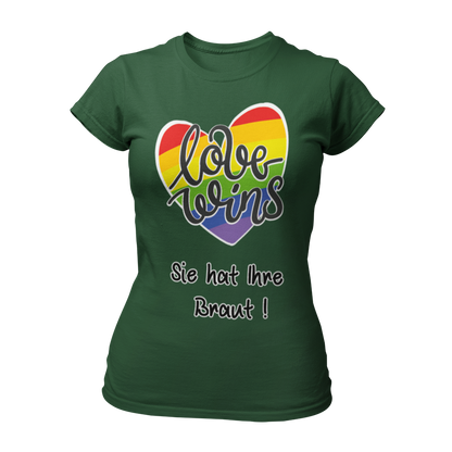 Damen T-Shirt "Love wins! Sie hat Ihre Braut!" im Regenbogen-Look, mit verspieltem Schriftzug „love wins“ auf einem herzförmigen Hintergrund. Das Shirt feiert die gleichgeschlechtliche Ehe und betont mit dem zusätzlichen Slogan „Sie hat ihre Braut!“, dass hier zwei Frauen heiraten. Hergestellt aus hochwertigem Material mit Doppelnähten, ist es ein ideales, figurbetontes JGA-Shirt für einen bunten und offenen Junggesellinnenabschied.