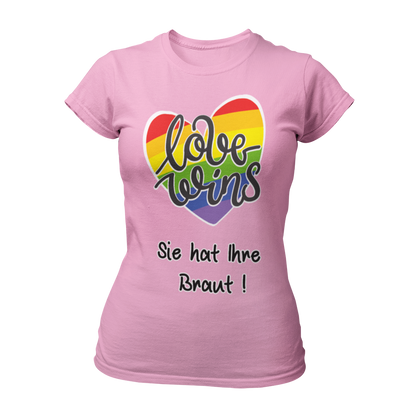 Damen T-Shirt "Love wins! Sie hat Ihre Braut!" im Regenbogen-Look, mit verspieltem Schriftzug „love wins“ auf einem herzförmigen Hintergrund. Das Shirt feiert die gleichgeschlechtliche Ehe und betont mit dem zusätzlichen Slogan „Sie hat ihre Braut!“, dass hier zwei Frauen heiraten. Hergestellt aus hochwertigem Material mit Doppelnähten, ist es ein ideales, figurbetontes JGA-Shirt für einen bunten und offenen Junggesellinnenabschied.