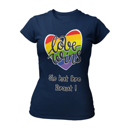 Damen T-Shirt "Love wins! Sie hat Ihre Braut!" im Regenbogen-Look, mit verspieltem Schriftzug „love wins“ auf einem herzförmigen Hintergrund. Das Shirt feiert die gleichgeschlechtliche Ehe und betont mit dem zusätzlichen Slogan „Sie hat ihre Braut!“, dass hier zwei Frauen heiraten. Hergestellt aus hochwertigem Material mit Doppelnähten, ist es ein ideales, figurbetontes JGA-Shirt für einen bunten und offenen Junggesellinnenabschied.