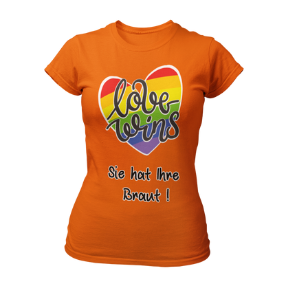 Damen T-Shirt "Love wins! Sie hat Ihre Braut!" im Regenbogen-Look, mit verspieltem Schriftzug „love wins“ auf einem herzförmigen Hintergrund. Das Shirt feiert die gleichgeschlechtliche Ehe und betont mit dem zusätzlichen Slogan „Sie hat ihre Braut!“, dass hier zwei Frauen heiraten. Hergestellt aus hochwertigem Material mit Doppelnähten, ist es ein ideales, figurbetontes JGA-Shirt für einen bunten und offenen Junggesellinnenabschied.