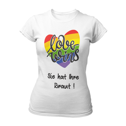 Damen T-Shirt "Love wins! Sie hat Ihre Braut!" im Regenbogen-Look, mit verspieltem Schriftzug „love wins“ auf einem herzförmigen Hintergrund. Das Shirt feiert die gleichgeschlechtliche Ehe und betont mit dem zusätzlichen Slogan „Sie hat ihre Braut!“, dass hier zwei Frauen heiraten. Hergestellt aus hochwertigem Material mit Doppelnähten, ist es ein ideales, figurbetontes JGA-Shirt für einen bunten und offenen Junggesellinnenabschied.