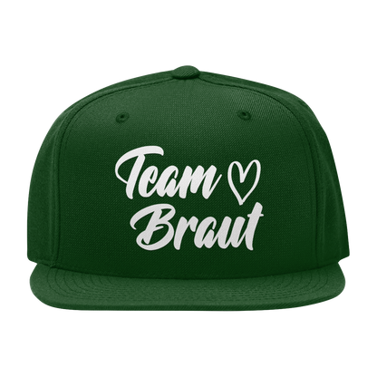 JGA Cap „Team Braut – Herzen“ mit flachem Schirm und vier gestickten Ösen. Die Kappe ist mit einer „Team Braut“ Aufschrift und Herzmotiven auf der Vorderseite bedruckt. Der PVC-Verschluss auf der Rückseite ist größenverstellbar, was eine individuelle Anpassung ermöglicht. Diese Premium JGA-Kappe ist das perfekte Accessoire für die Begleiterinnen der Braut.