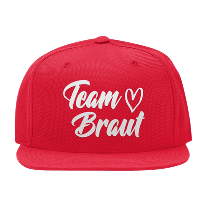 JGA Cap „Team Braut – Herzen“ mit flachem Schirm und vier gestickten Ösen. Die Kappe ist mit einer „Team Braut“ Aufschrift und Herzmotiven auf der Vorderseite bedruckt. Der PVC-Verschluss auf der Rückseite ist größenverstellbar, was eine individuelle Anpassung ermöglicht. Diese Premium JGA-Kappe ist das perfekte Accessoire für die Begleiterinnen der Braut.