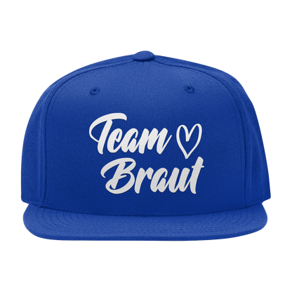 JGA Cap „Team Braut – Herzen“ mit flachem Schirm und vier gestickten Ösen. Die Kappe ist mit einer „Team Braut“ Aufschrift und Herzmotiven auf der Vorderseite bedruckt. Der PVC-Verschluss auf der Rückseite ist größenverstellbar, was eine individuelle Anpassung ermöglicht. Diese Premium JGA-Kappe ist das perfekte Accessoire für die Begleiterinnen der Braut.