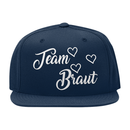 JGA Cap „Team Braut“ mit flachem Schirm und roten „Team Braut“ Schriftzug sowie Herzen auf der Vorderseite. Die Kappe hat vier gestickte Ösen für Belüftung und einen größenverstellbaren PVC-Verschluss auf der Rückseite.