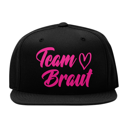 JGA Cap „Team Braut – Herzen“ mit flachem Schirm und vier gestickten Ösen. Die Kappe ist mit einer „Team Braut“ Aufschrift und Herzmotiven auf der Vorderseite bedruckt. Der PVC-Verschluss auf der Rückseite ist größenverstellbar, was eine individuelle Anpassung ermöglicht. Diese Premium JGA-Kappe ist das perfekte Accessoire für die Begleiterinnen der Braut.