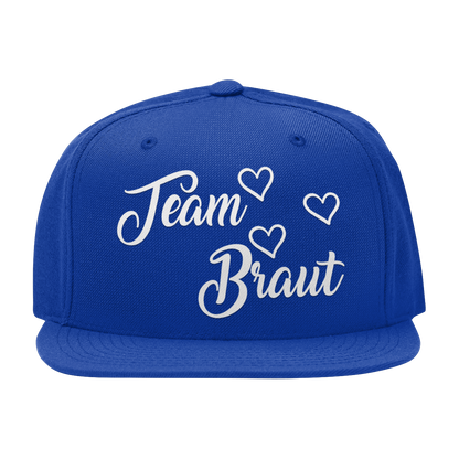 JGA Cap „Team Braut“ mit flachem Schirm und roten „Team Braut“ Schriftzug sowie Herzen auf der Vorderseite. Die Kappe hat vier gestickte Ösen für Belüftung und einen größenverstellbaren PVC-Verschluss auf der Rückseite.